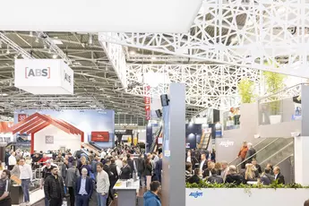 Blick in eine Halle der BAU 2025. Besucher stehen um viele unterschiedliche Stände herum. An der Decke sieht man eine kunstvolle Konstruktion aus weißen Streben.