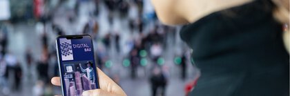 Eine Frau hält ein Handy in der Hand, auf der die App der digitalBAU geöffnet ist