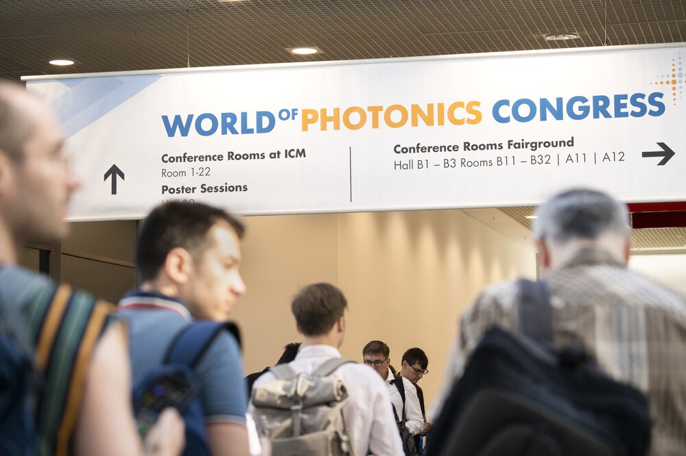People walk through a busy corridor with a signpost for the World of Photonics Congress.
