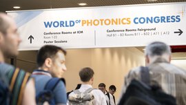 People walk through a busy corridor with a signpost for the World of Photonics Congress.