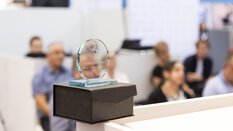 Glass trophy of the Investors Choice Award on the edge of a table. Spectators are blurred in the background.