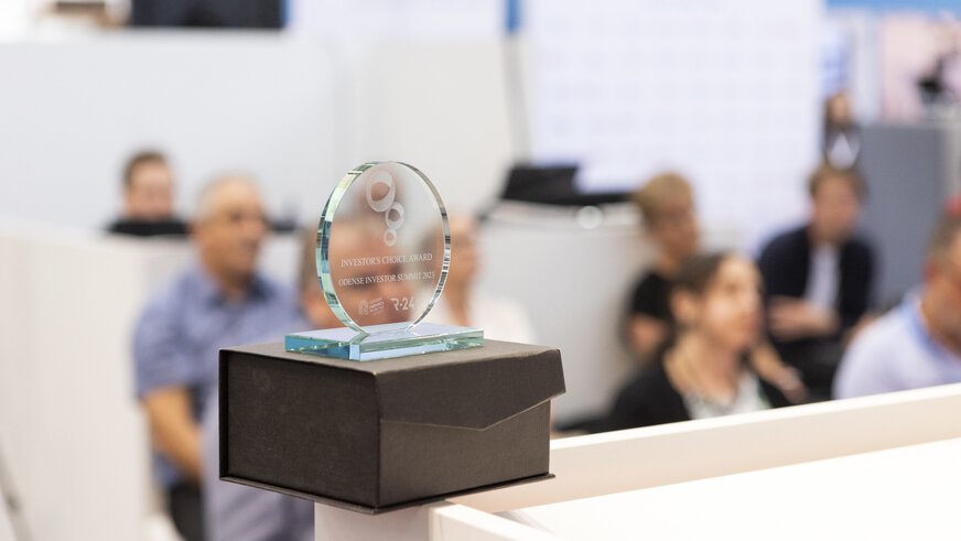 Glass trophy of the Investors Choice Award on the edge of a table. Spectators are blurred in the background.