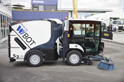 Side view of a compact road sweeper parked on asphalt in an open area.