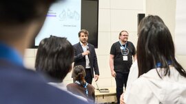 Eröffnung eines Workshops auf der World of Quantum 2025 in München: Zwei Referenten begrüßen die Teilnehmenden vor einer Präsentation zum Thema 