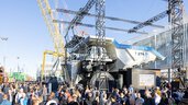 Large crowd around a huge mining lorry, cranes and structures in the background at the outdoor areas of Messe München.