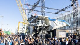 Large crowd around a huge mining lorry, cranes and structures in the background at the outdoor areas of Messe München.