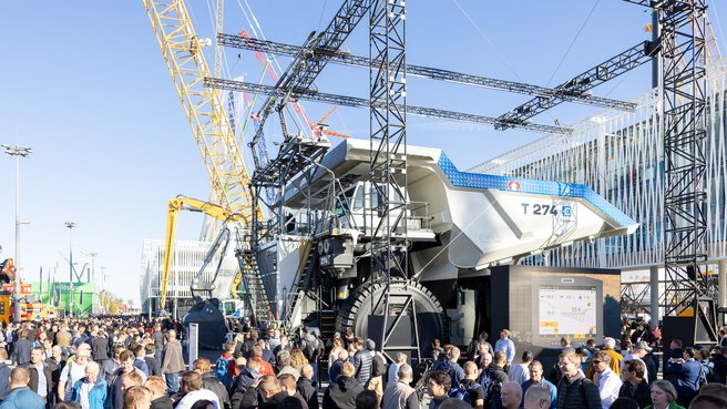 Large crowd around a huge mining lorry, cranes and structures in the background at the outdoor areas of Messe München.