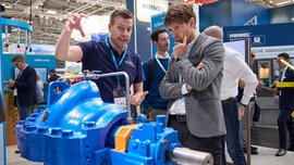 An expert at the Xylem stand explains a large, bright blue industrial pump to an interested visitor.