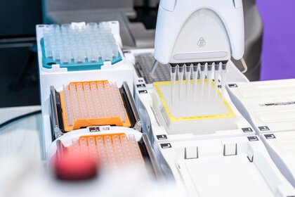 An automated pipetting station precisely dispenses liquids into a laboratory plate with multiple rows of reaction vessels.