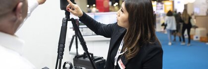 An exhibitor demonstrates a surveying device to a visitor at an exhibition stand.