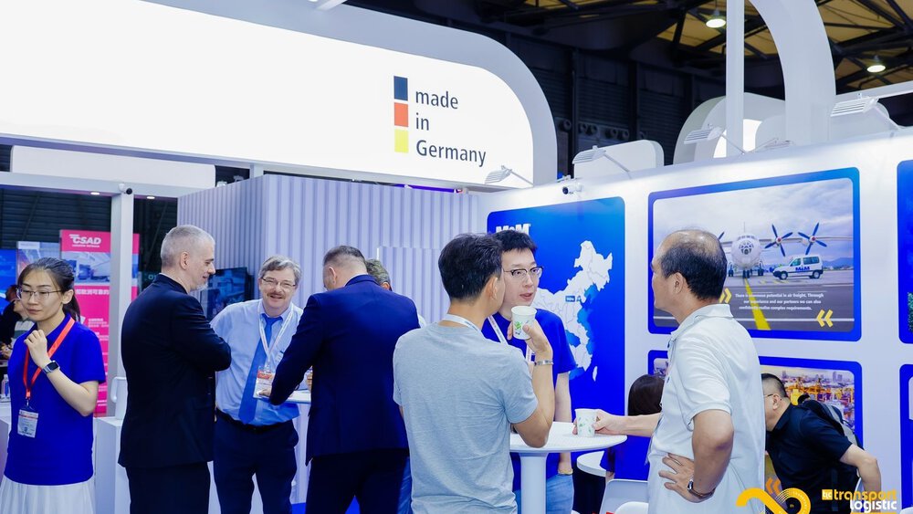 Besucher an einem Stand der transport logistic CHINA diskutieren an Stehtischen. Darüber ist ein Banner mit dem Slogan 