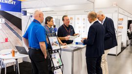 Five men are standing at a stand at transport logistic Americas, discussing the contents of a flyer that one of them is holding.