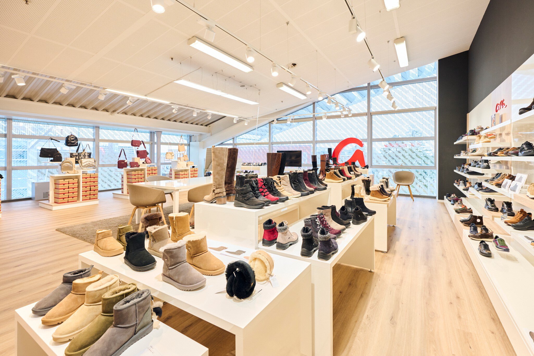 Ein großer heller Ausstellungsraum mit Glasfensterfronten und einem schrägen Dach. Auf Tischen und in Regalen werden Schuhe präsentiert.