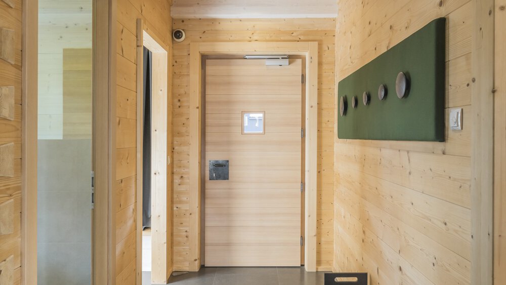 Ein Flur mit Holzwänden, einem grünen Schild und einer geschlossenen Holztür am Ende.