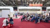 Vortrag auf der „Reisebühne“ der Messe f.re.e mit großem Publikum, roten Teppichen und umliegenden Reiseständen in einer Messehalle.