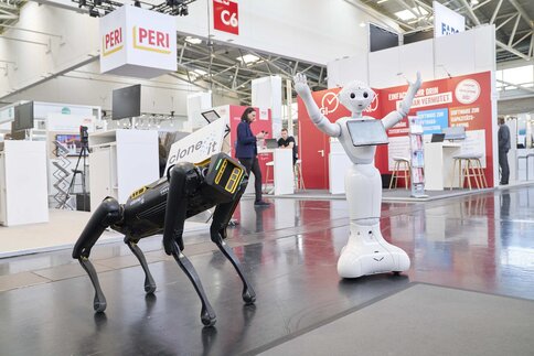 Ein Roboterhund und ein humanoider Roboter posieren vor einem Messestand.