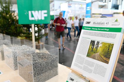 Focus on a pile of leaflets at the stand of the Bavarian State Institute for Forestry and Forest Economics, next to transparent containers with different types of gravel.