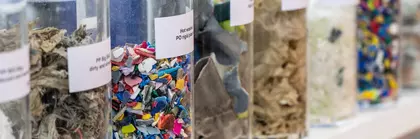 Transparent cylinders lined up, labeled and filled with various recycled materials.