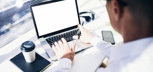 Person in a bright business environment using a laptop with a blank screen and holding a pen.