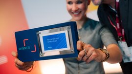 Zwei Personen präsentieren einen Preis oder Award vor einer Kamera auf der DMEA