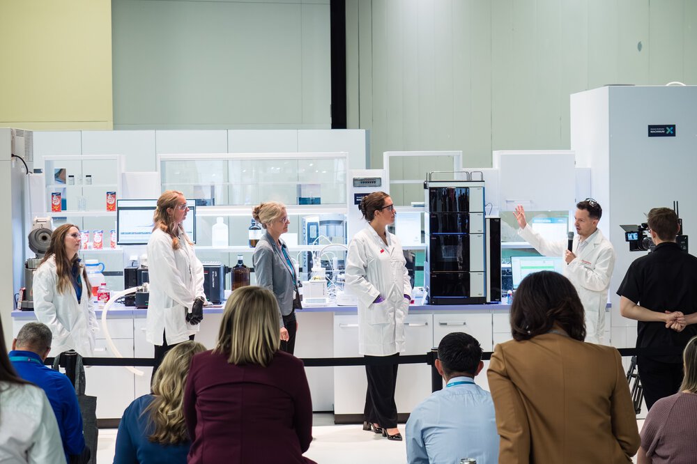 A group of scientists in lab coats presenting to an audience in a modern laboratory environment.