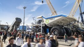 Menschenmenge auf einer Messe vor einem riesigen Muldenkipper und Baumaschinen unter blauem Himmel.