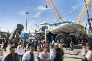 Menschenmenge auf einer Messe vor einem riesigen Muldenkipper und Baumaschinen unter blauem Himmel.