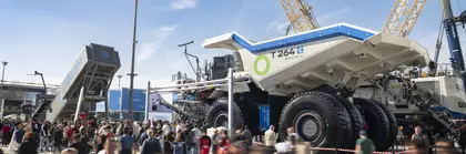 Menschenmenge auf einer Messe vor einem riesigen Muldenkipper und Baumaschinen unter blauem Himmel.