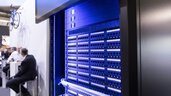 Blue illuminated server rack with numerous connection sockets on the wall of an exhibition stand.