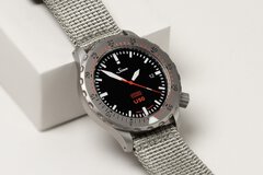 A close-up view of a wristwatch with a black dial, minute markers on the outer edge, and a fabric strap.