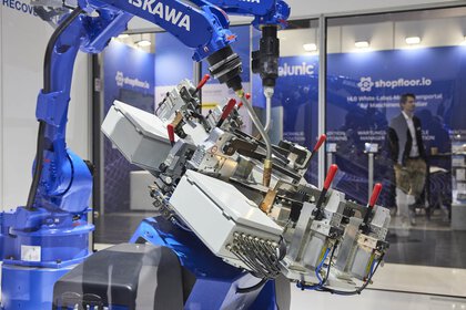 A blue industrial robot arm at an exhibition stand interacting with complex electronic parts.