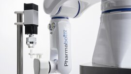 Roboterarm mit der Aufschrift „Pharmabotix“ und einem Greifwerkzeug, positioniert neben einem kleinen zylindrischen Gerät.