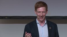 Ein lächelnder Redner mit Headset gestikuliert während einer Präsentation.