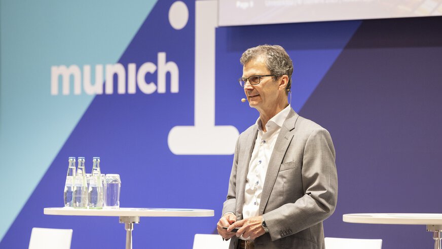 A man in a gray suit speaks on stage at munich_i.