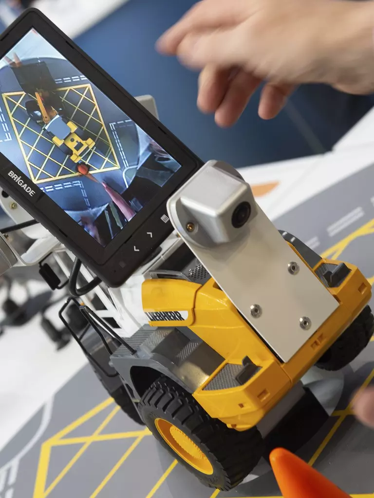 One person controls a small robot with wheels and a screen that shows a map.