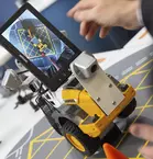 One person controls a small robot with wheels and a screen that shows a map.