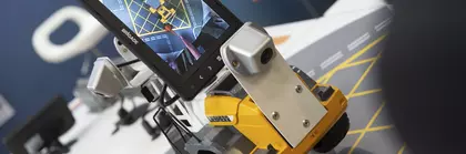 Eine Person steuert einen kleinen Roboter mit Rädern und Bildschirm, der eine Karte zeigt.
