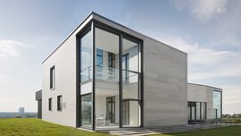 Modern two-story house with large glass windows and clean, minimalist design, set on a lawn.
