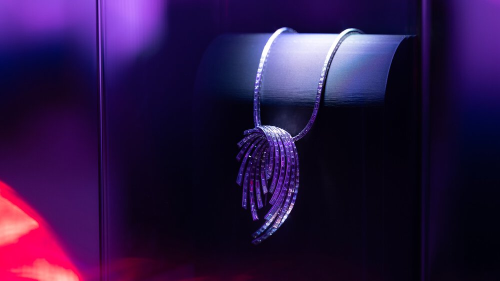A silver statement necklace with a geometric pendant, presented under purple light.