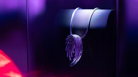 A silver statement necklace with a geometric pendant, presented under purple light.