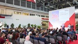 Ein Zuschauerbereich mit großem Publikum, welches dem Vortrag eines Mannes auf einer Bühne der ceramitec zuhört.