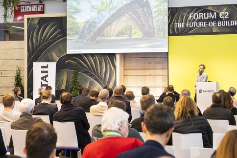 Ein Mann hält während der BAU-Messe vor einem aufmerksamen sitzenden Publikum einen Vortrag.