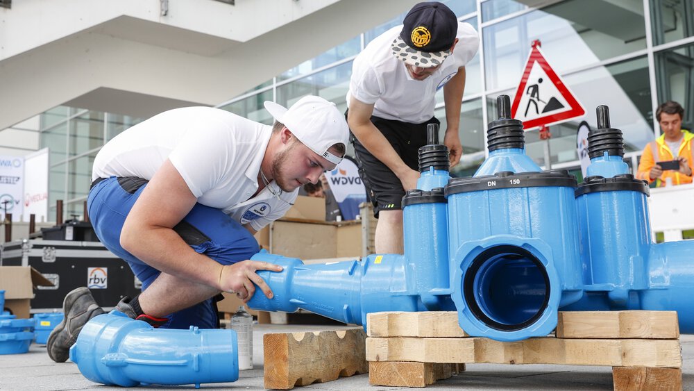 Two workers install a complex pipe system as part of a demonstration in front of an exhibition hall.