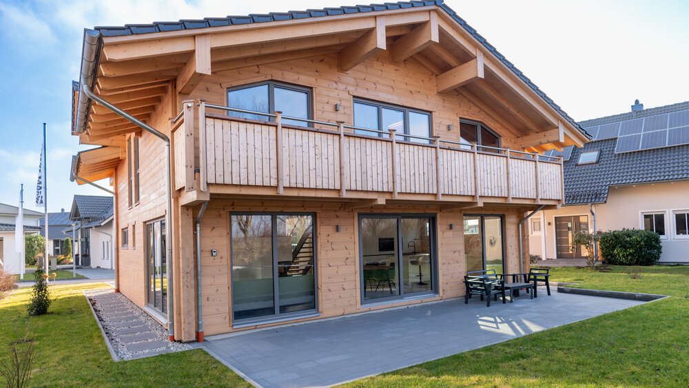 Ein zweistöckiges Holzhaus mit großem Balkon und Terrasse, auf dem Ausstellungsgelände des Bauzentrum Poing.