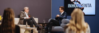 Two men in suits are sitting in armchairs on a stage at INHORGENTA, chatting in front of an audience.