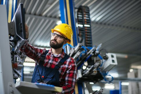 Mann mit Schutzhelm und Brille bedient Maschinen in einer Industrieanlage.