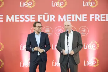 Two men stand on a stage in front of a screen at an opening ceremony.