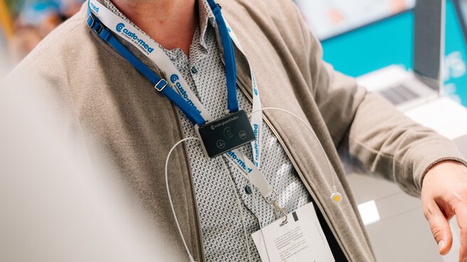 Close-up of a wearable medical device with electrodes and badge holder at a DMEA booth