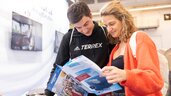 Two people smile as they look at brochures at an event or trade fair booth.