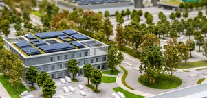 Miniaturmodell eines modernen dreistöckigen Bürogebäudes mit Solarmodulen, Bäumen und Parkplatz in einer städtischen Umgebung.